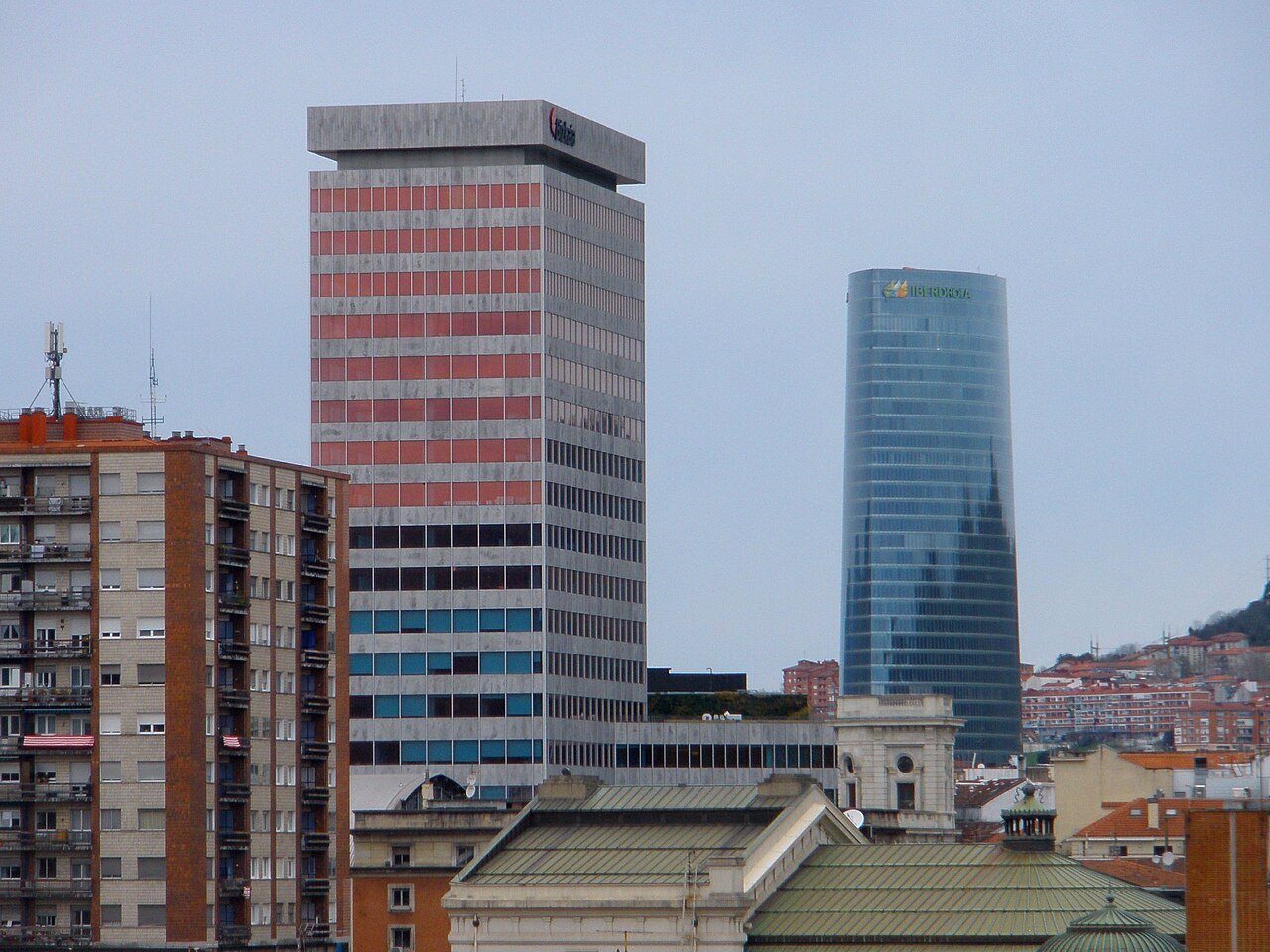An older office block with striped windows beside the curved glass of the Iberdrola Tower