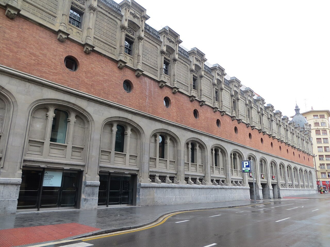 The long side wall of Azkuna Zentroa, brick above a stone base, on a wet day