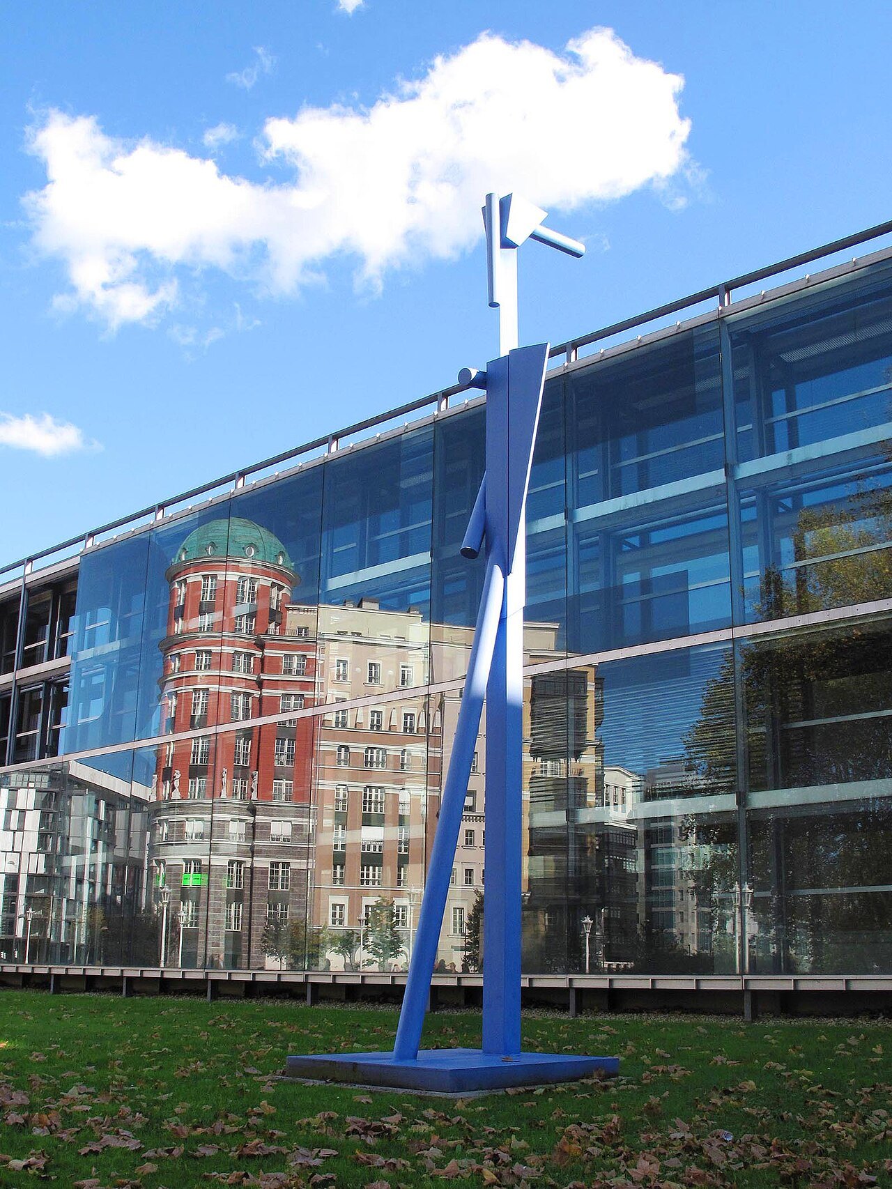 A tall blue sculpture on the lawn before a mirrored glass building