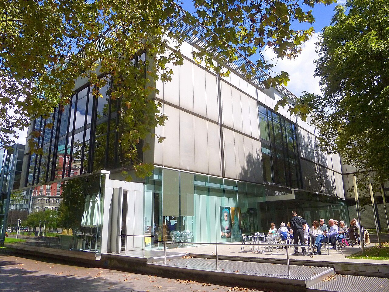 The glass wing of the Fine Arts Museum under the trees, visitors gathered at its entrance