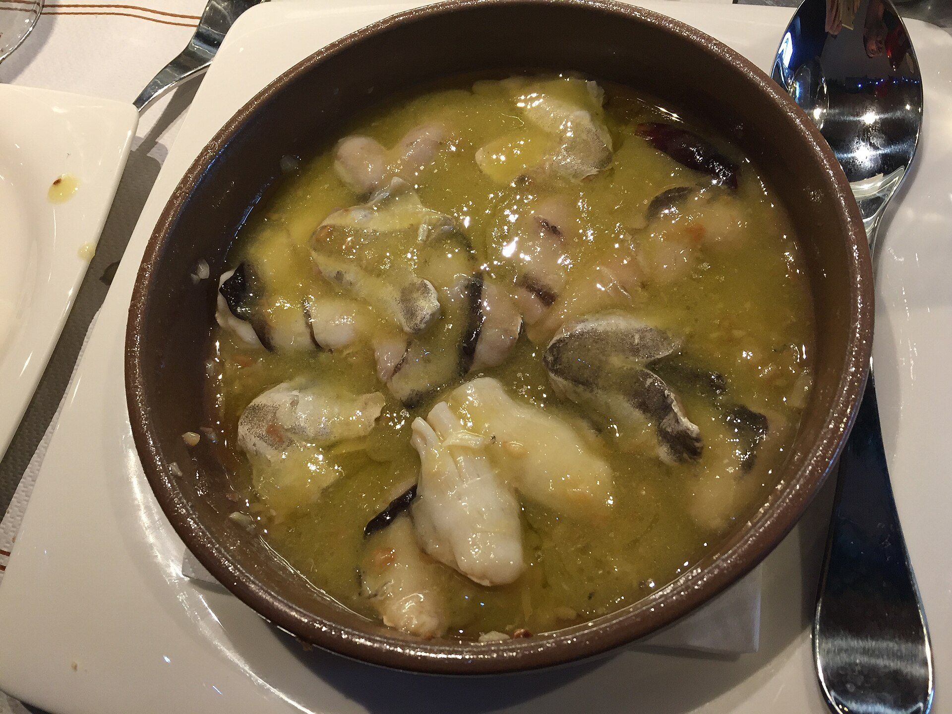 Kokotxas, hake throats, in a pale pil pil sauce in an earthenware dish
