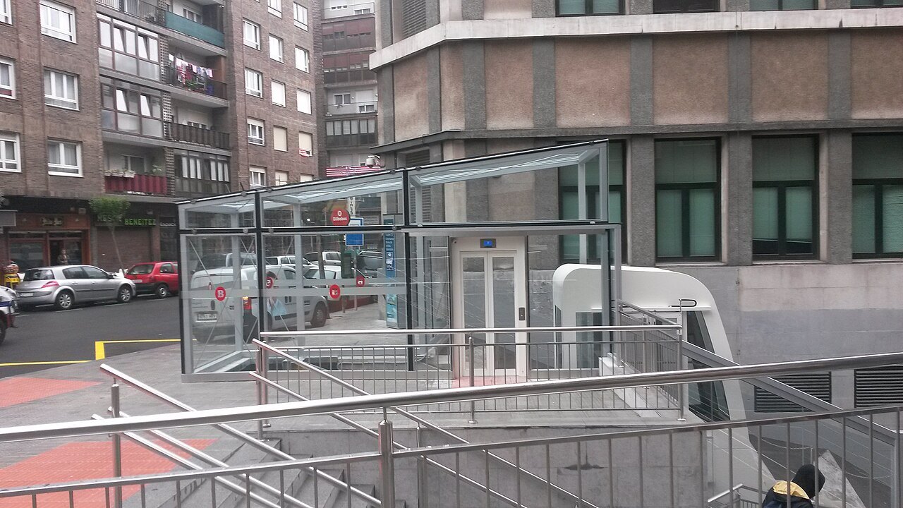 The glass head of the public lift at Iturribide, between apartment blocks