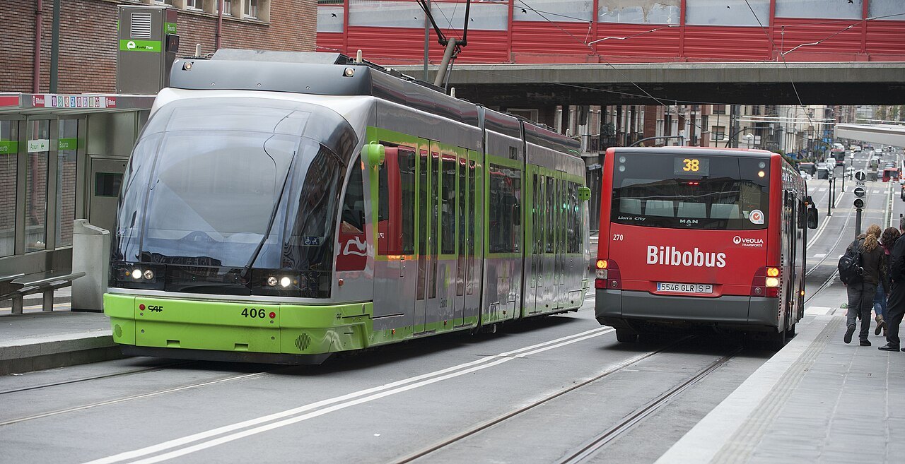 A green tram and a red Bilbobus side by side at Basurto