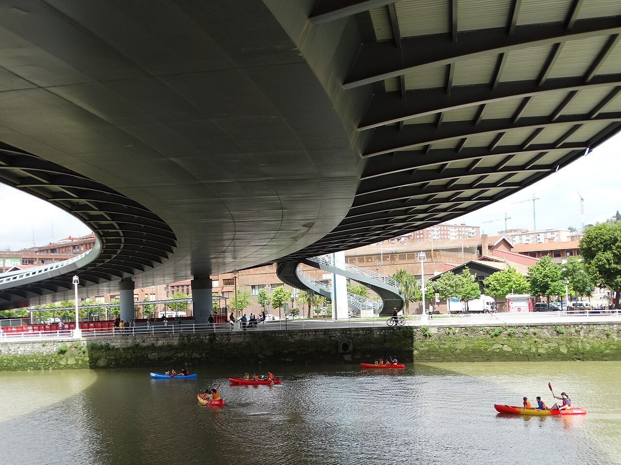 Kayakers paddling under the curving deck of the Euskalduna bridge