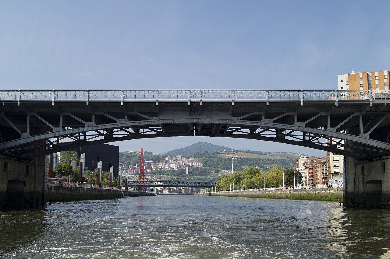 The Deusto bridge seen from the water, the red arch of La Salve framed beneath it