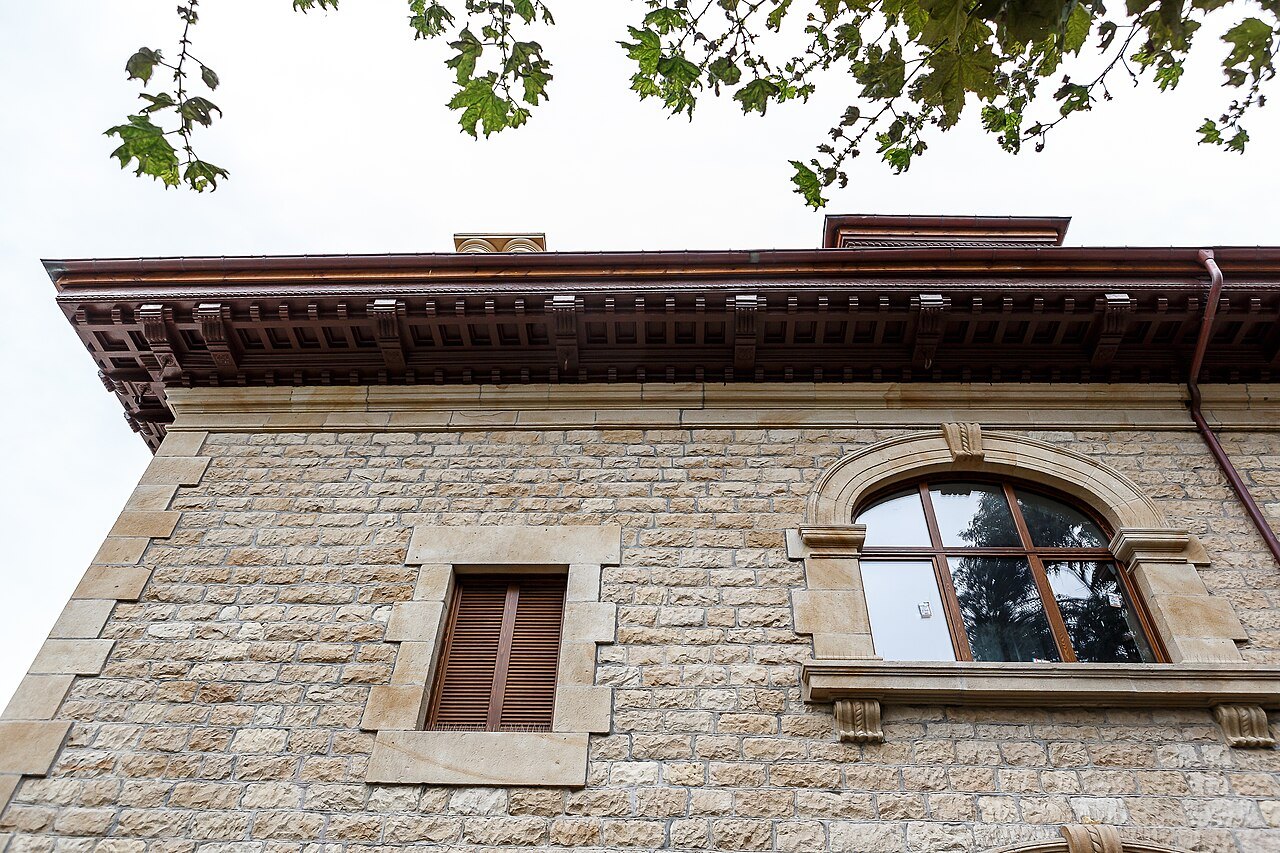 Deep carved eaves and an arched window on a stone villa in Neguri