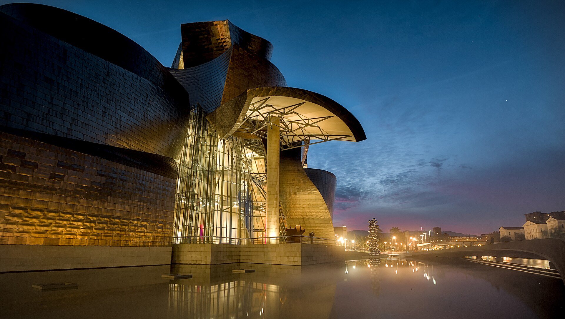 The Guggenheim lit at dusk, its glass atrium glowing between titanium curves