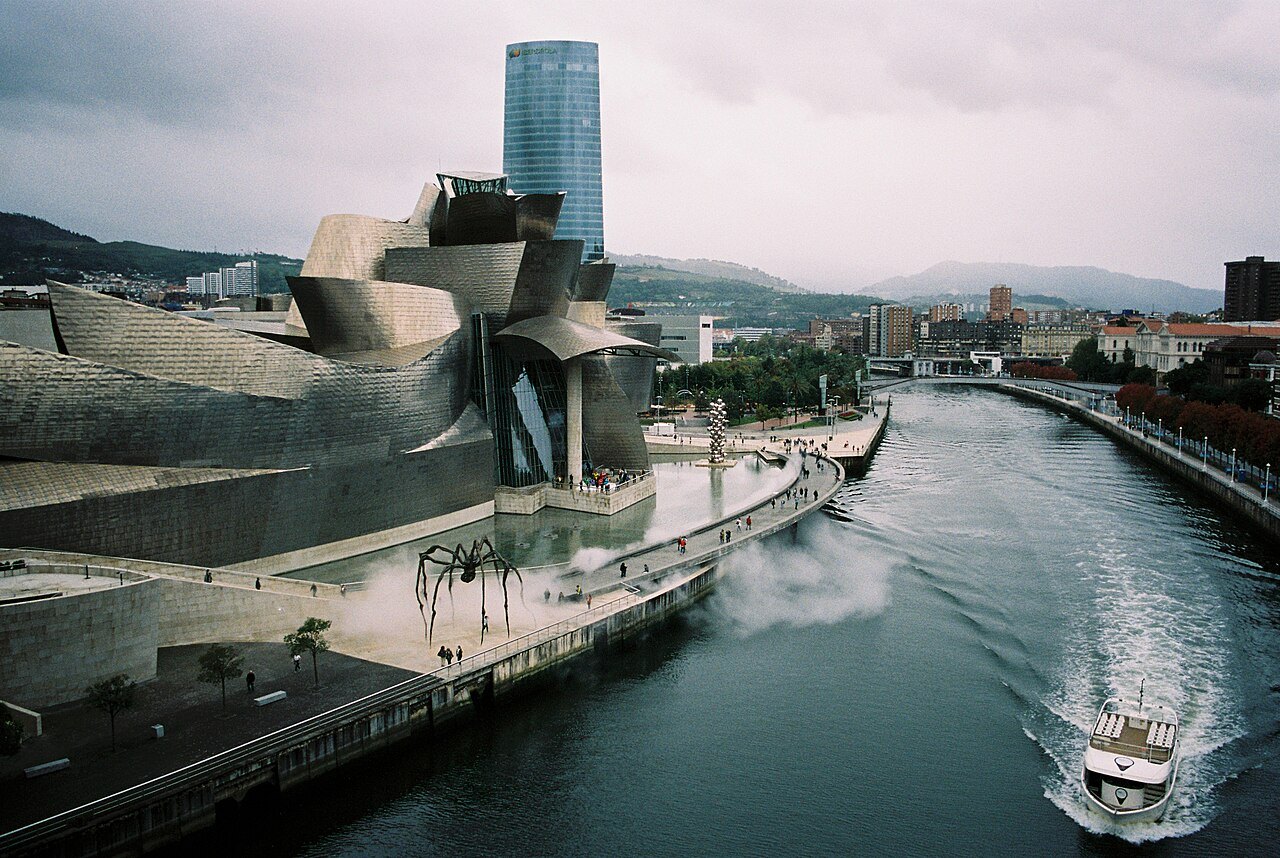 A boat speeding past the Guggenheim on the river, the Iberdrola Tower behind