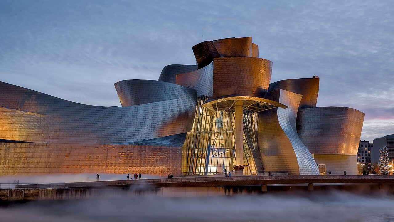 The Guggenheim's titanium at dusk, lights glowing behind its glass atrium