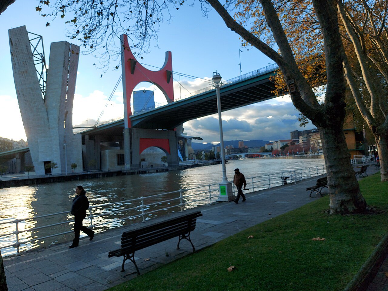 Walkers on the riverbank below La Salve bridge and its stair tower