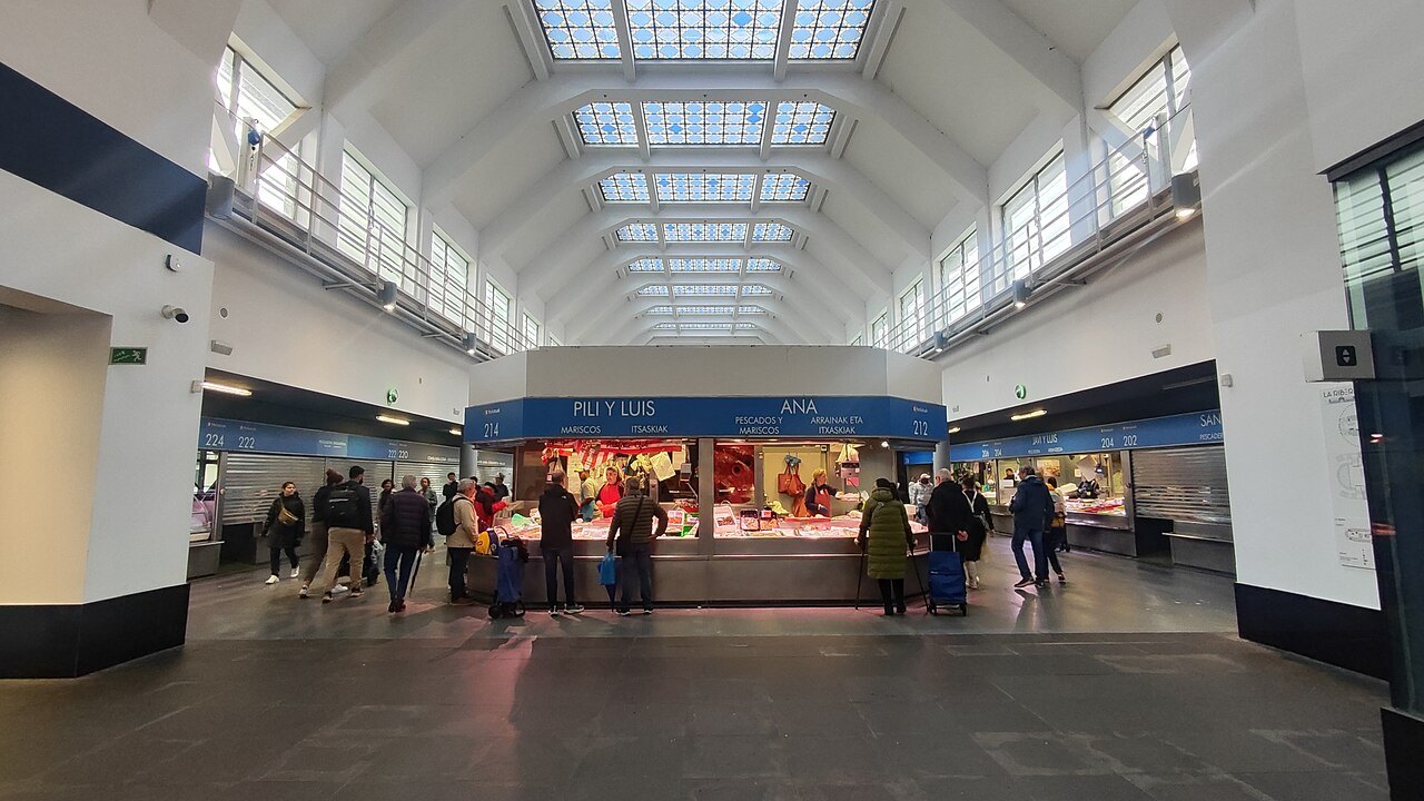 Shoppers at the stalls under the white vaulted roof of the Ribera market