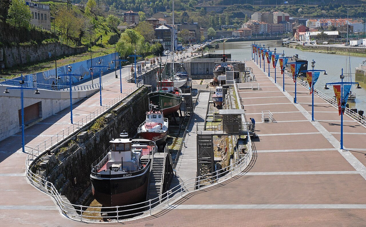 Boats displayed in the old dry dock beside the Itsasmuseum, flags along the quay