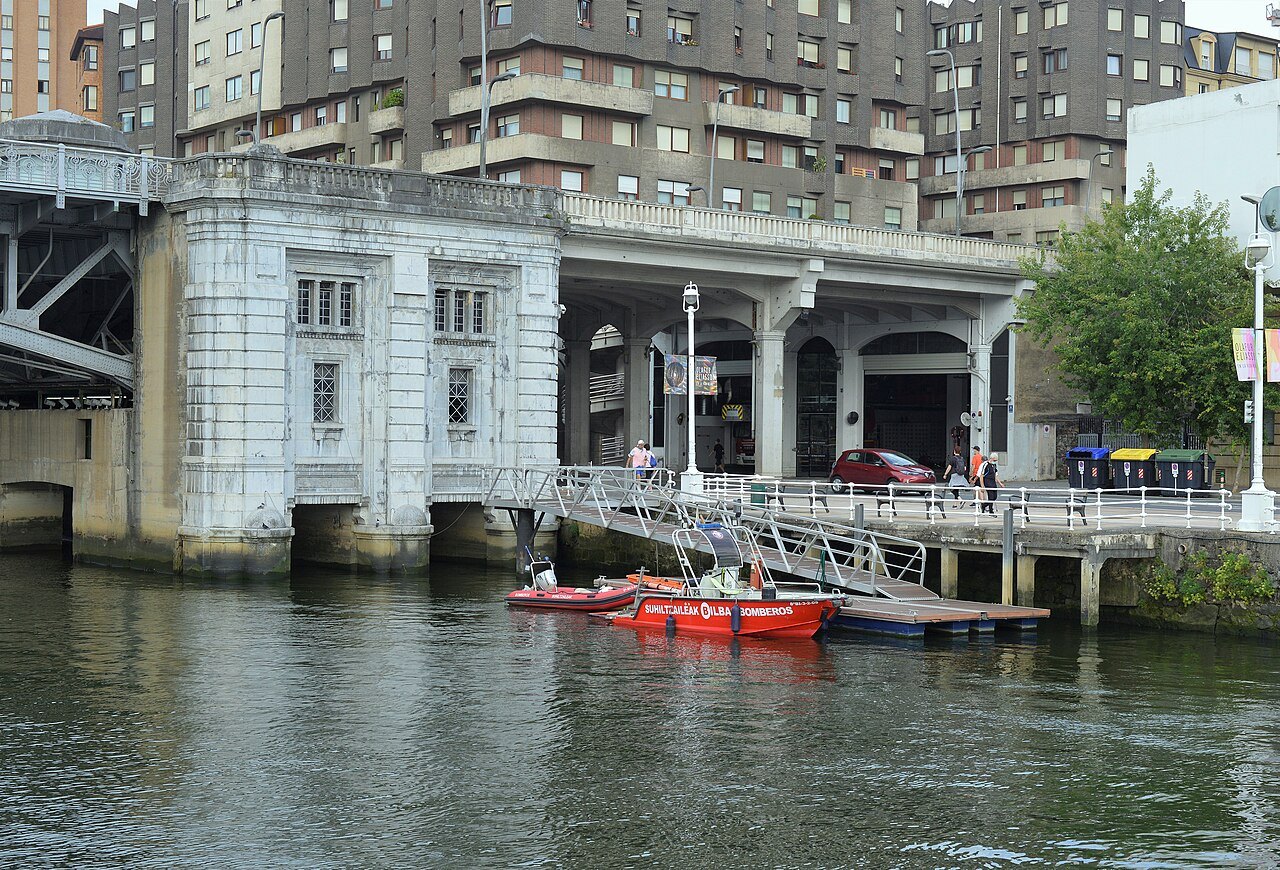 The old machinery house of the Deusto bridge, red boats moored below