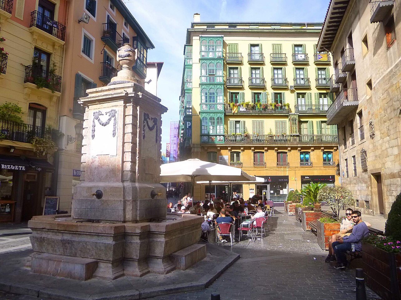 The stone fountain of the Plaza de Santiago, café tables around it