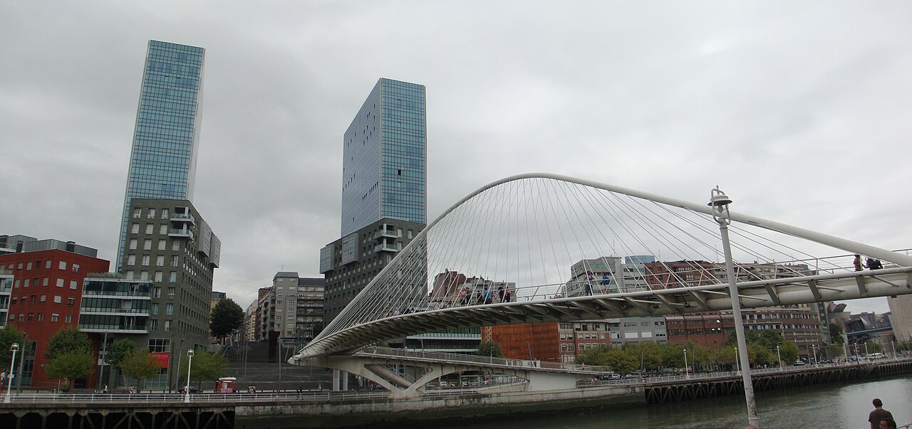Zubizuri spanning the river under a gray sky, the Isozaki towers on the left bank